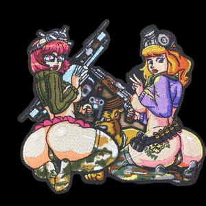 Op de afbeelding: Geborduurde patch met twee stripvrouwen met wapens. De ene vrouw heeft roze haar en een bril, de andere is blond. Beide dragen kleding in militaire stijl. De patch heeft een zwarte achtergrond.