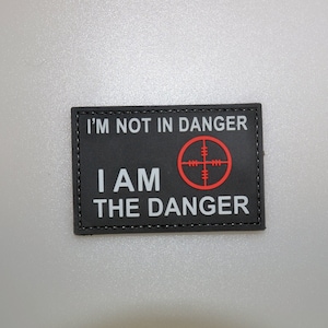 May include: Black rectangular patch with white text: "I'M NOT IN DANGER I AM THE DANGER." A red crosshair graphic is on the right. The patch has a black border and is likely made of fabric.