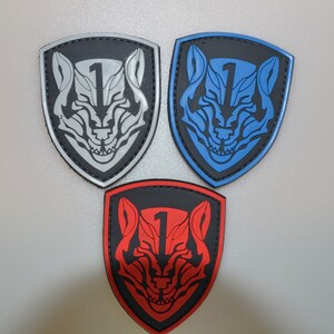 以下が含まれることがあります： オオカミの頭のデザインと数字の1が入った、シールド型のパッチが3つ。1つは黒地にグレー、もう1つは黒地に青、3つ目は黒地に赤です。これらのパッチは、おそらく衣類やアクセサリー用です。