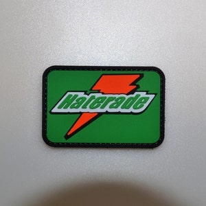 Könnte beinhalten: Ein rechteckiger Aufnäher mit grünem Hintergrund und dem Wort "Haterade" in Weiß, umrandet in Grün, mit einem orangefarbenen Blitzdesign. Der Aufnäher hat einen schwarzen Rand.