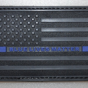May include: Black rectangular patch featuring a stylized American flag design. The flag's stars are embossed, and the stripes are horizontal. The text "BLUE LIVES MATTER" is in blue, with a blue stripe. The patch has a stitched border.