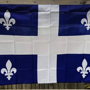 Puede incluir: Una bandera rectangular con un diseño azul y blanco. La bandera tiene una cruz blanca en el centro, con cuatro símbolos de flor de lis blancos en cada esquina. La bandera está hecha de una tela ligera.