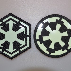 Puede incluir: Dos parches negros y verde claro. Uno es un hexágono con un diseño de estrella de seis puntas verde claro. El otro es un círculo con un diseño de estrella de ocho puntas verde claro. Ambos parches tienen un borde negro.