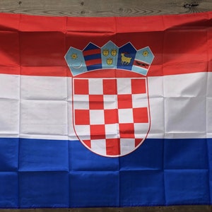 Puede incluir: Bandera rectangular de Croacia, con franjas horizontales rojas, blancas y azules. El escudo de armas croata está centrado, con un escudo ajedrezado rojo y blanco. La bandera está hecha de un material ligero.