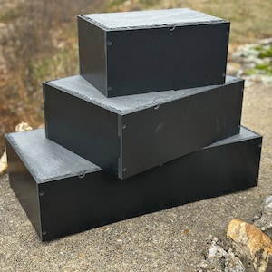 K&ouml;nnte beinhalten: Drei schwarze rechteckige Boxen, die &uuml;bereinander gestapelt sind. Die Boxen sind aus einem Material, das wie Schiefer aussieht.