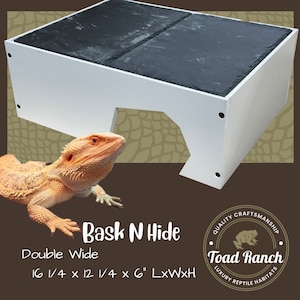 K&ouml;nnte beinhalten: Ein wei&szlig;es Reptilienversteck mit einer schwarzen Schieferplatte oben. Das Versteck ist h&ouml;hlenf&ouml;rmig mit einer gro&szlig;en &Ouml;ffnung. Das Versteck ist 41,3 cm lang, 31,1 cm breit und 15,2 cm hoch. Der Text "Bask N Hide" und "Double Wide" ist auf der Vorderseite des Verstecks aufgedruckt. Der Text "QUALITY CRAFTSMANSHIP" und "Toad Ranch" ist auf einem Kreis mit einer Kr&ouml;tenillustration aufgedruckt. Der Text "LUXURY REPTILE HABITATS" ist unter dem Kreis aufgedruckt.