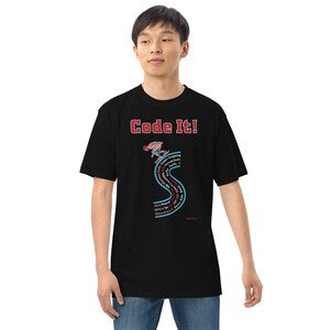 Pode incluir: Camiseta preta com o texto "Code It!" em vermelho e branco. A camiseta apresenta um gráfico de uma pessoa praticando snowboard em uma forma de "S" estilizada com termos de programação. A camiseta também inclui o texto "Java, Pascal, C, C++, Objective-C, Basic e App".
