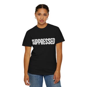 May include: Black t-shirt with the word "SUPPRESSED" printed in distressed white lettering. The shirt is a classic crew neck style and is being worn by a person in blue jeans.