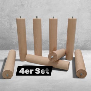 May include: A set of eight cylindrical light-coloured wooden furniture legs, each featuring a small metal threaded bolt protruding from one end. The legs are arranged in a group, with some standing upright and others lying horizontally on the surface.