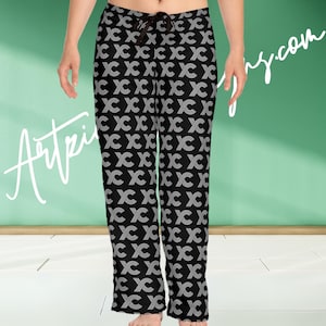 Puede incluir: Pantalones de pijama negros con un patrón blanco repetido de "XC". Los pantalones tienen una cintura con cordón. La imagen también incluye el texto "Artpin" y "y.com" en el fondo.