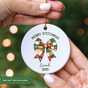 May include: White ceramic Christmas ornament with a watercolor bow design in green, red, and tan. The ornament reads "MERRY STITCHMAS" and includes the name "Sarah" and the year "2025".