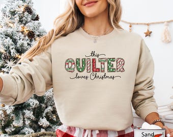 Può includere: Felpa beige con la scritta "this QUILTER loves Christmas". La parola "QUILTER" è disegnata con motivi festivi rossi e verdi. Un capo stagionale per gli appassionati di quilting.