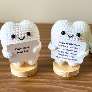 May include: Two white crochet tooth plushies with black eyes, pink cheeks, and a smiling mouth. One holds a sign that says "Customize Your Text." The other holds a sign that says "Happy Tooth Plush...You are awesome!!"