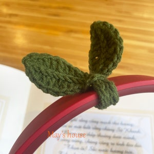 May include: Green crocheted leaf-shaped headphone charms. The charms are attached to a red headphone band.