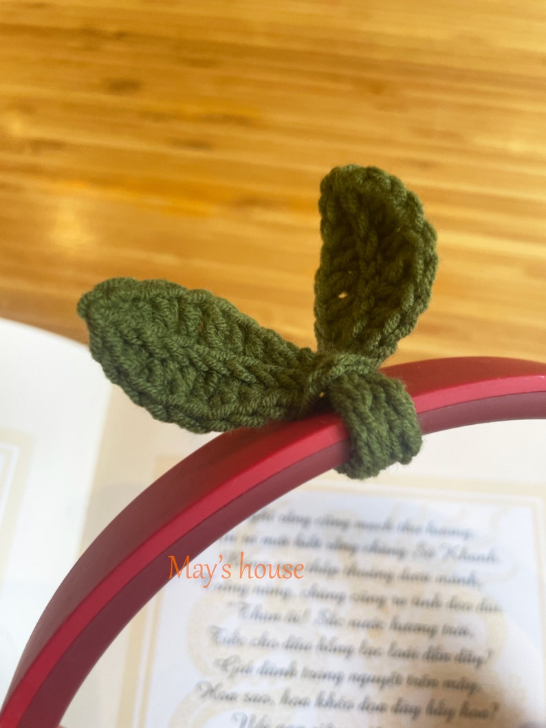 May include: Green crocheted leaf-shaped headphone charms. The charms are attached to a red headphone band.
