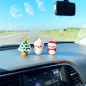 May include: Three small, crocheted Christmas ornaments: a green tree, a pink-hatted snowman, and a snowman with a red hat and scarf. The ornaments are displayed on a car dashboard. The text "May's house" is visible.