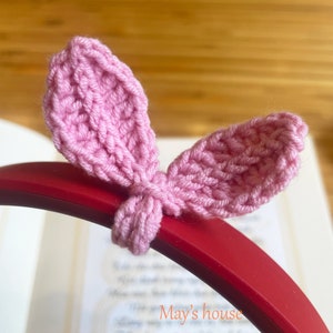 May include: Pink crocheted bunny ear headband for headphones. The headband is on a red headphone band. The text "May's house" is visible in the background.