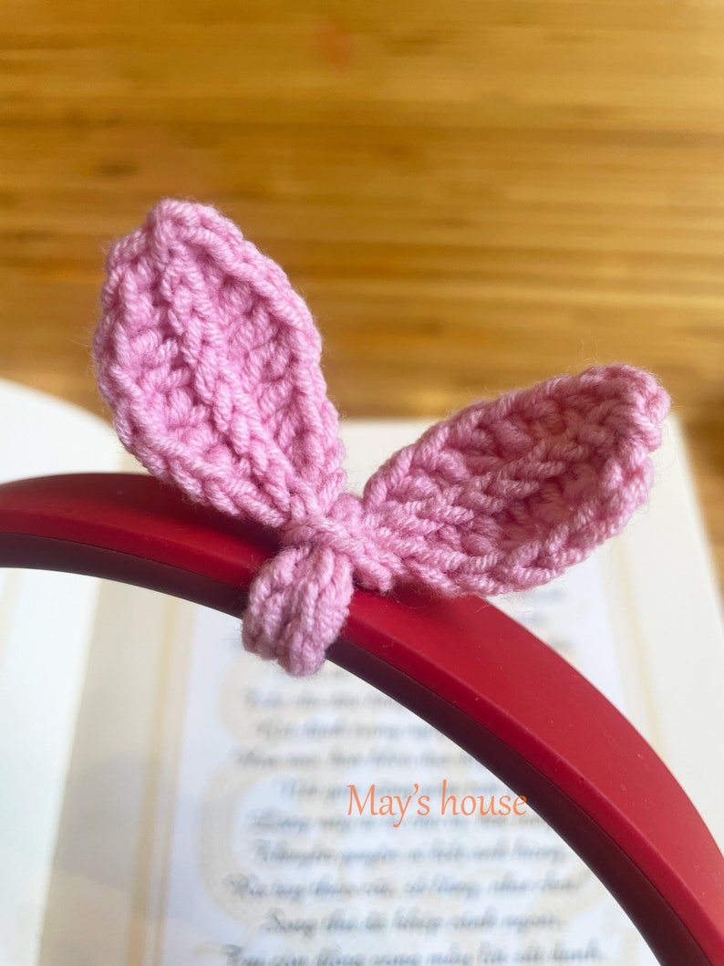 May include: Pink crocheted bunny ear headband for headphones. The headband is on a red headphone band. The text "May's house" is visible in the background.