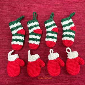 May include: Set of eight crocheted Christmas ornaments, including five red and white striped stockings and three red mittens with white cuffs. The ornaments are arranged on a red fabric background.