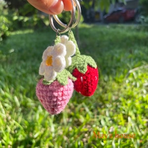May include: A crocheted strawberry keyring with a white flower. The keyring is attached to a silver key ring.