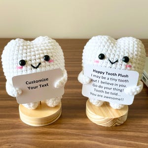May include: Two white crocheted tooth plushies with black eyes and pink cheeks. Each tooth holds a sign; one says "Customize Your Text," the other says "Happy Tooth Plush...You are awesome!!" They sit on wooden bases.