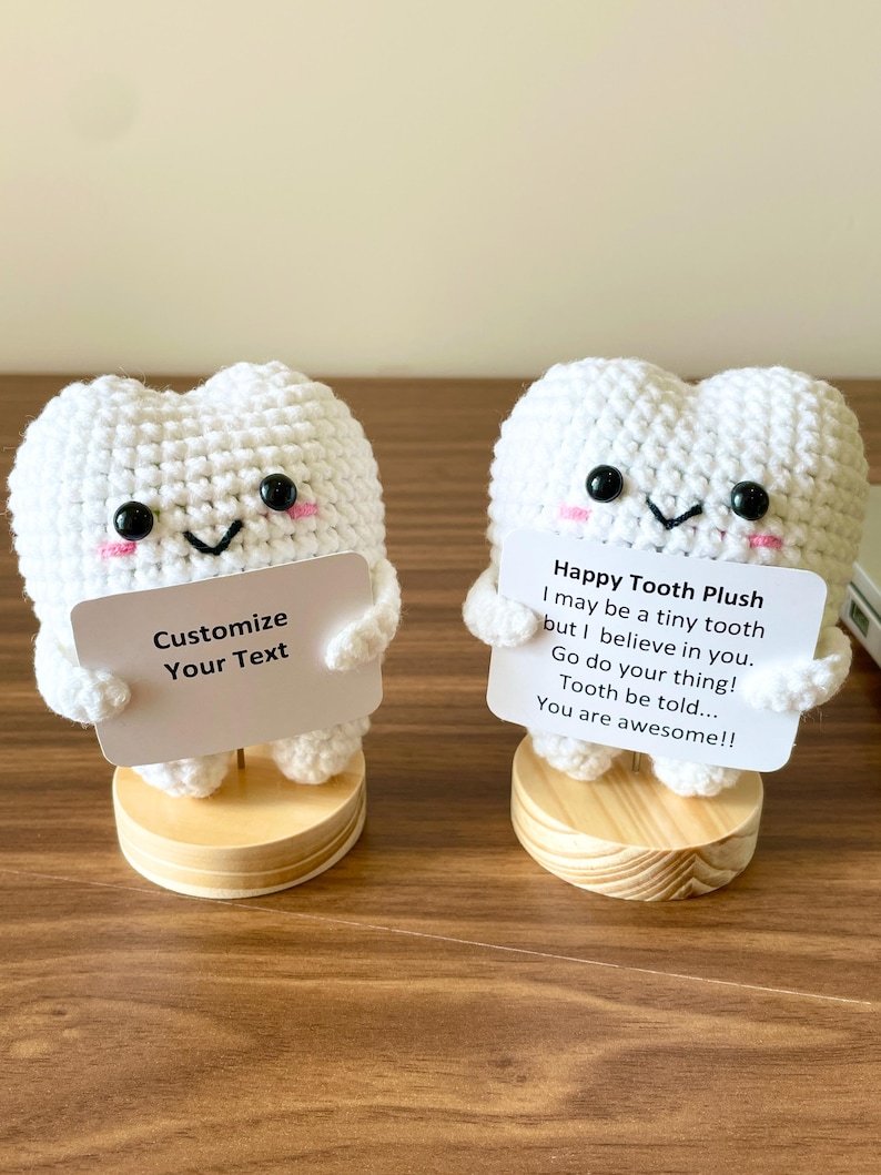 May include: Two white crocheted tooth plushies with black eyes and pink cheeks. Each tooth holds a sign; one says "Customize Your Text," the other says "Happy Tooth Plush...You are awesome!!" They sit on wooden bases.