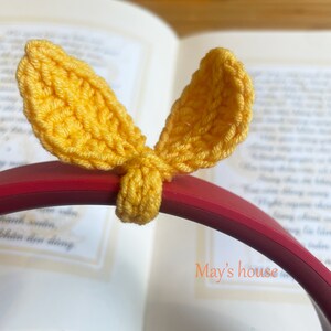 May include: Yellow crocheted bunny ear shaped headphone covers on a red headband. The text "May's house" is visible in the background.
