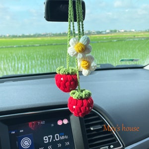 May include: A handmade car charm featuring two red crocheted strawberries with green tops and two white daisy flowers with yellow centers. The charm hangs from a green crocheted cord. The text "May's house" is visible.