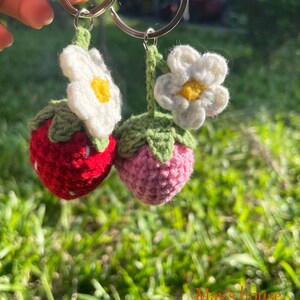 May include: Two crocheted strawberry keyrings with white flowers. The strawberries are red and pink.