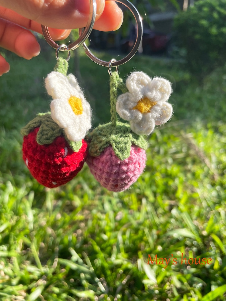 May include: Two crocheted strawberry keyrings with white flowers. The strawberries are red and pink.