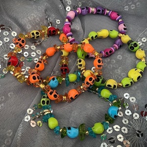 Könnte beinhalten: Ein Set aus bunten Totenkopf-Perlenarmbändern mit verschiedenen farbigen Perlen und Charms. Die Armbänder sind aus Kunststoff und auf elastischem Band aufgefädelt.