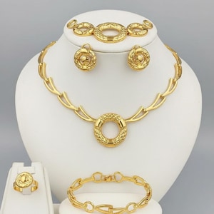 May include: A complete gold-toned jewelry set displayed on a white mannequin. The set includes a necklace, bracelet, earrings, ring, and a matching bracelet. The necklace and ring feature a textured circular design. The jewelry is displayed against a neutral background.