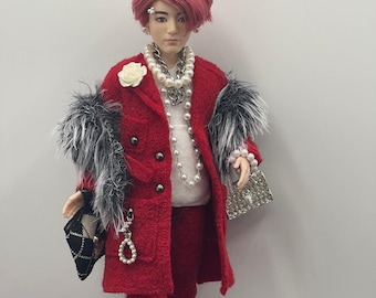 May include: A fashion doll dressed in a red suit with a matching coat, white sneakers, and a pearl necklace. The doll has red hair and is accessorized with a black and white patterned purse and a silver clutch. The coat features black and white fur trim.