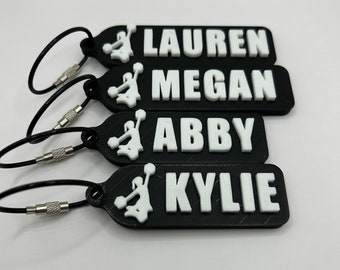 May include: Four black keychains with white cheerleaders and names "Lauren", "Megan", "Abby", and "Kylie" printed on them.
