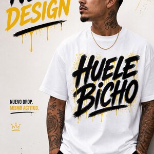 May include: A white short-sleeved t-shirt featuring black graffiti-style text that reads HUELE BICHO with yellow paint splatter accents. The shirt is paired with black shorts. The image includes the text NEW DESIGN and NUEVO DROP. MISMO ACTITUD.