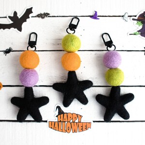 K&ouml;nnte beinhalten: Drei Halloween-Zipper-Anh&auml;nger mit schwarzen Filzsternen und Filzkugeln in Orange, Gr&uuml;n und Lila.