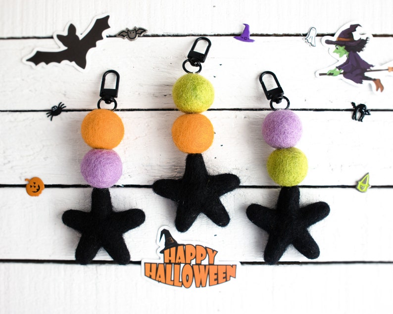 K&ouml;nnte beinhalten: Drei Halloween-Zipper-Anh&auml;nger mit schwarzen Filzsternen und Filzkugeln in Orange, Gr&uuml;n und Lila.