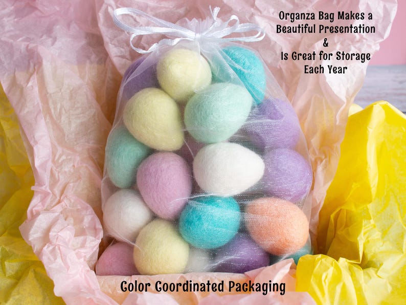 May include: A sheer organza bag filled with pastel coloured felt Easter eggs. The bag is sitting on a pink and yellow tissue paper background. The text "Organza Bag Makes a Beautiful Presentation & Is Great for Storage Each Year" is written above the bag. The text "Color Coordinated Packaging" is written below the bag.