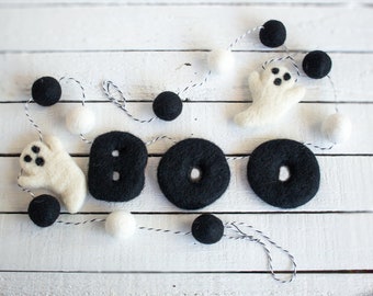 May include: A Halloween garland with the word "BOO" spelled out in black felt letters. The garland also features white felt ghost shapes and black and white pom-poms strung along a white and black twine.