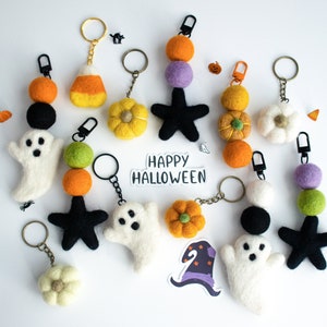 K&ouml;nnte beinhalten: Eine Sammlung von Halloween-Schl&uuml;sselanh&auml;ngern aus Filz mit Geistern, Sternen, K&uuml;rbissen, Zuckermais und Blumen. Die Schl&uuml;sselanh&auml;nger sind an goldenen Ketten befestigt und haben schwarze und wei&szlig;e Filzaugen. Der Text "Happy Halloween" ist auf einem wei&szlig;en Aufkleber geschrieben.