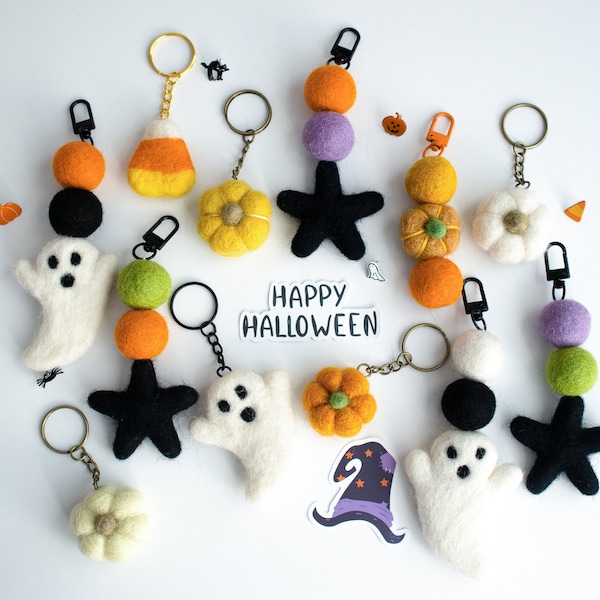 以下が含まれることがあります： ゴースト、星、カボチャ、キャンディーコーン、花など、ハロウィーンをテーマにしたフェルト製のキーホルダーのコレクションです。キーホルダーは金色のチェーンに通されており、黒と白のフェルトの目があります。白いステッカーに「Happy Halloween」の文字が書かれています。