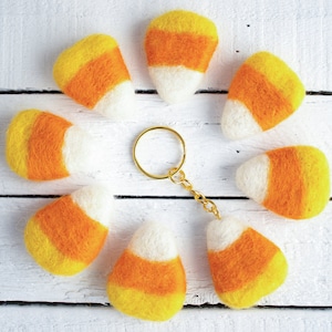 K&ouml;nnte beinhalten: Ein Set aus acht Schl&uuml;sselanh&auml;ngern aus Filz in Form von Maisbonbons in Orange, Gelb und Wei&szlig;. Die Schl&uuml;sselanh&auml;nger sind in einem Kreis um einen goldenen Schl&uuml;sselring angeordnet.