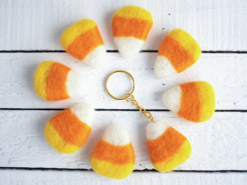 K&ouml;nnte beinhalten: Ein Set aus acht Schl&uuml;sselanh&auml;ngern aus Filz in Form von Maisbonbons in Orange, Gelb und Wei&szlig;. Die Schl&uuml;sselanh&auml;nger sind in einem Kreis um einen goldenen Schl&uuml;sselring angeordnet.