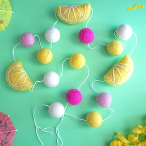 May include: A yellow and white felt lemon garland with pink and white felt balls. The garland is strung on white string and is perfect for a summer party or baby shower.