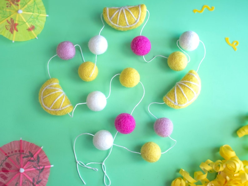 May include: A yellow and white felt lemon garland with pink and white felt balls. The garland is strung on white string and is perfect for a summer party or baby shower.