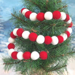 May include: Red and white felt ball garland draped around a Christmas tree. The garland is made of alternating red and white felt balls.