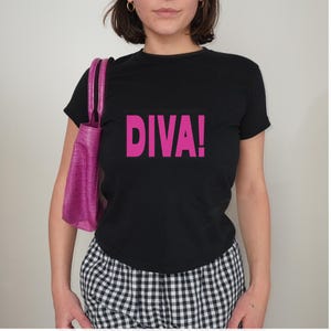 May include: A black short-sleeved t-shirt featuring the word DIVA! printed in bold pink capital letters across the chest, paired with a bright pink handbag with a textured crocodile-skin pattern and black and white checkered bottoms.