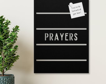May include: A black metal board with the word "PRAYERS" in silver lettering. The board has four horizontal lines and a white sticky note with the text "Trust in the Lord with all your heart." attached to the top line.