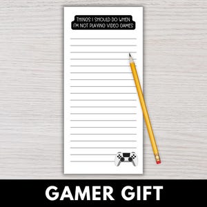 May include: A white notepad with horizontal lines, a black and white game controller graphic, and the text "THINGS I SHOULD DO WHEN I'M NOT PLAYING VIDEO GAMES". A yellow pencil rests on the notepad. The words "GAMER GIFT" are at the bottom.