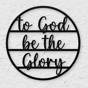 May include: Black metal circle wall decor with the words "to God be the glory" in a cursive font.